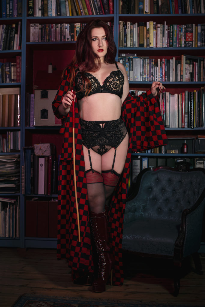 Miss Jessica Hyde in a library, dressed in red and black lingerie and carry a cane. 